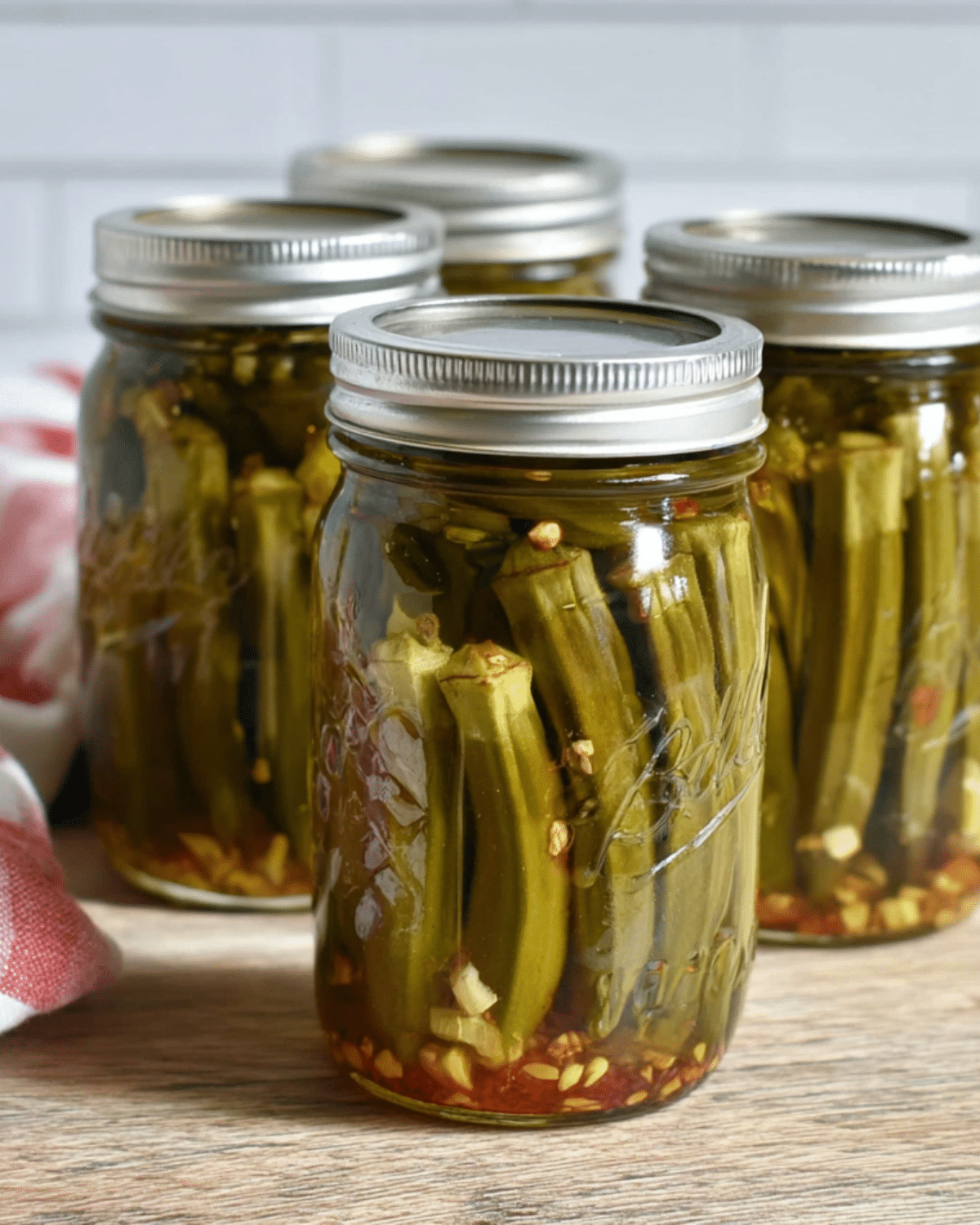 Jars of pickled okra in brine with garlic and spices, sealed with silver lids.