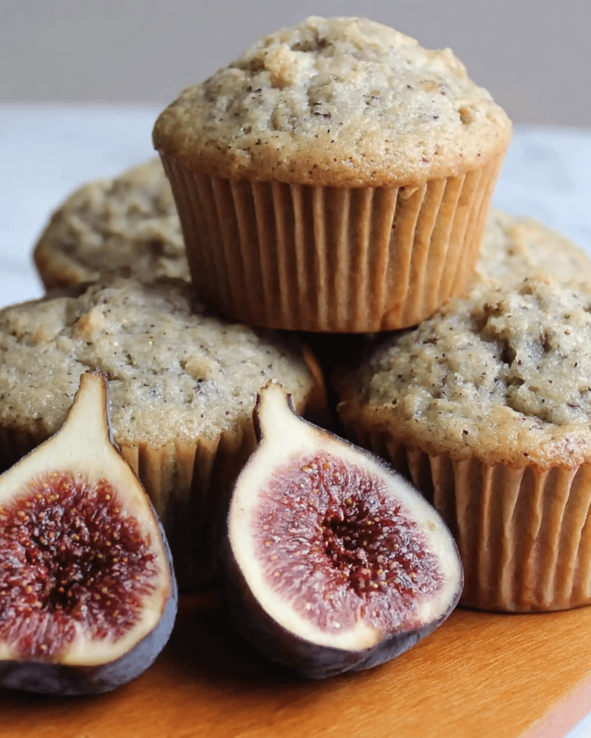 Freshly baked fig muffins stacked on a wooden surface with a ripe fig sliced in half in the foreground.