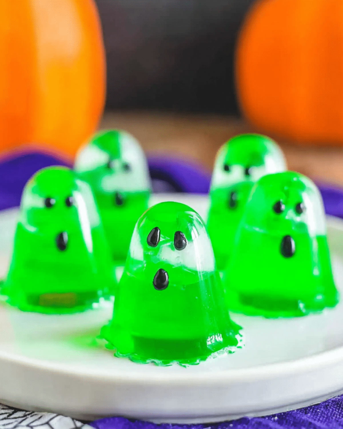 A plate of bright green ghost jello shots shaped like spooky little ghosts with black candy eyes and mouths.