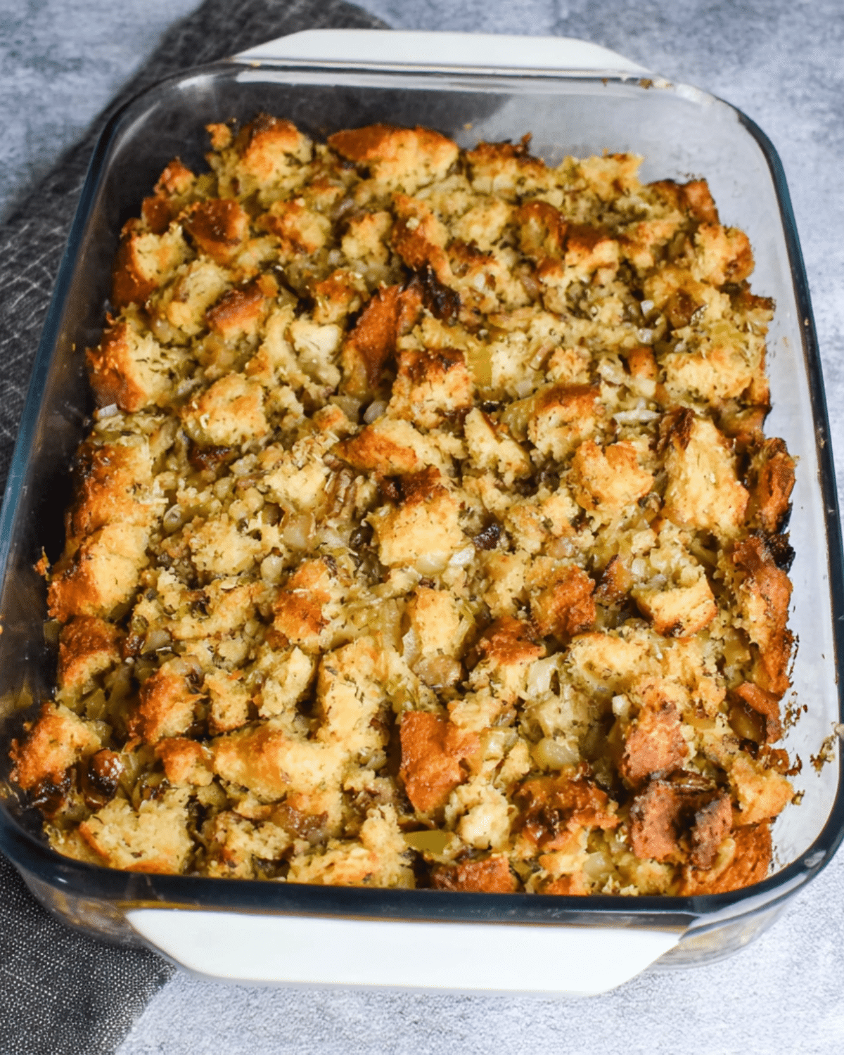 Grandma’s Thanksgiving Dressing baked golden brown in a glass casserole dish with chunks of bread, herbs, and vegetables.
