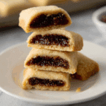 Stack of homemade fig Newtons with a golden cookie exterior and thick fig filling on a white plate.