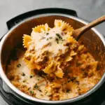Instant Pot lasagna with bowtie pasta, ground beef, marinara sauce, and melted cheese, scooped with a wooden spoon.