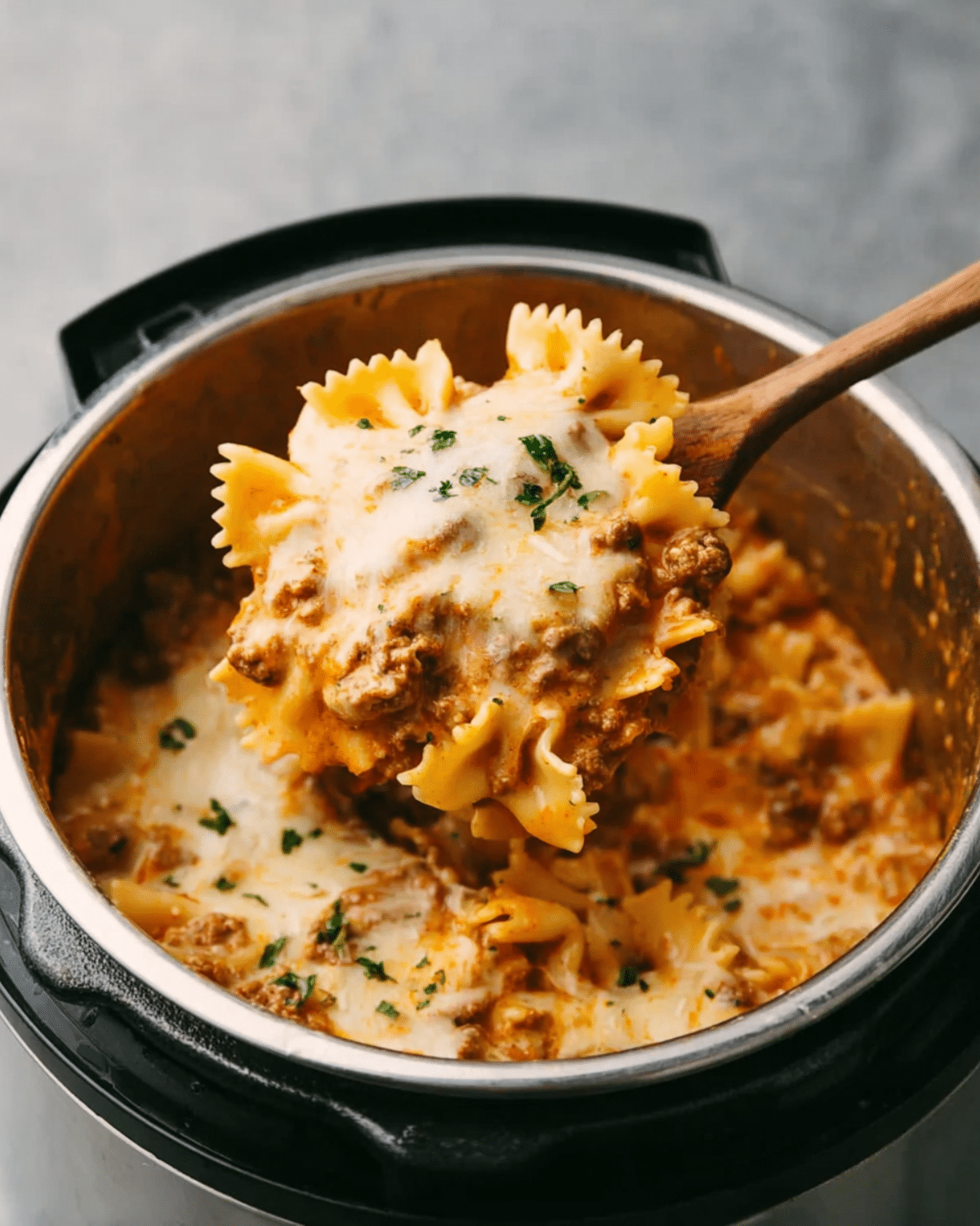 Instant Pot lasagna with bowtie pasta, ground beef, marinara sauce, and melted cheese, scooped with a wooden spoon.