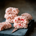 Marshmallow Rice Krispies Halloween Brains shaped like brains with pink and red tones, stacked on a black cutting board.