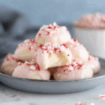 A plate of Peppermint Meltaways topped with crushed candy canes, with one cookie showing a bite taken out.