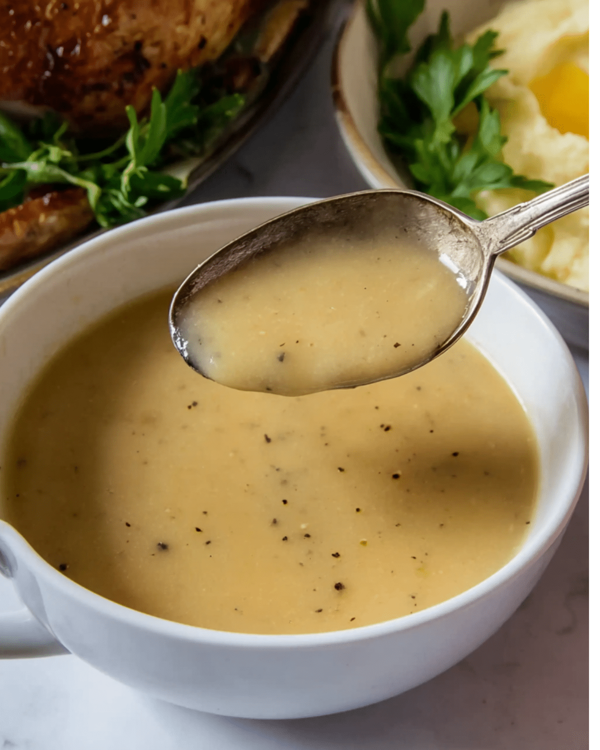 Perfect Turkey Gravy in a white bowl with a spoon lifting a portion, showing its smooth and creamy texture.