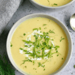 Potato Garlic Scape Soup served in a white bowl, garnished with fresh herbs, garlic scapes, and a swirl of cream.