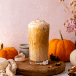 Pumpkin chai iced latte topped with creamy pumpkin foam and sprinkled with spices, served in a tall glass with autumn decor.