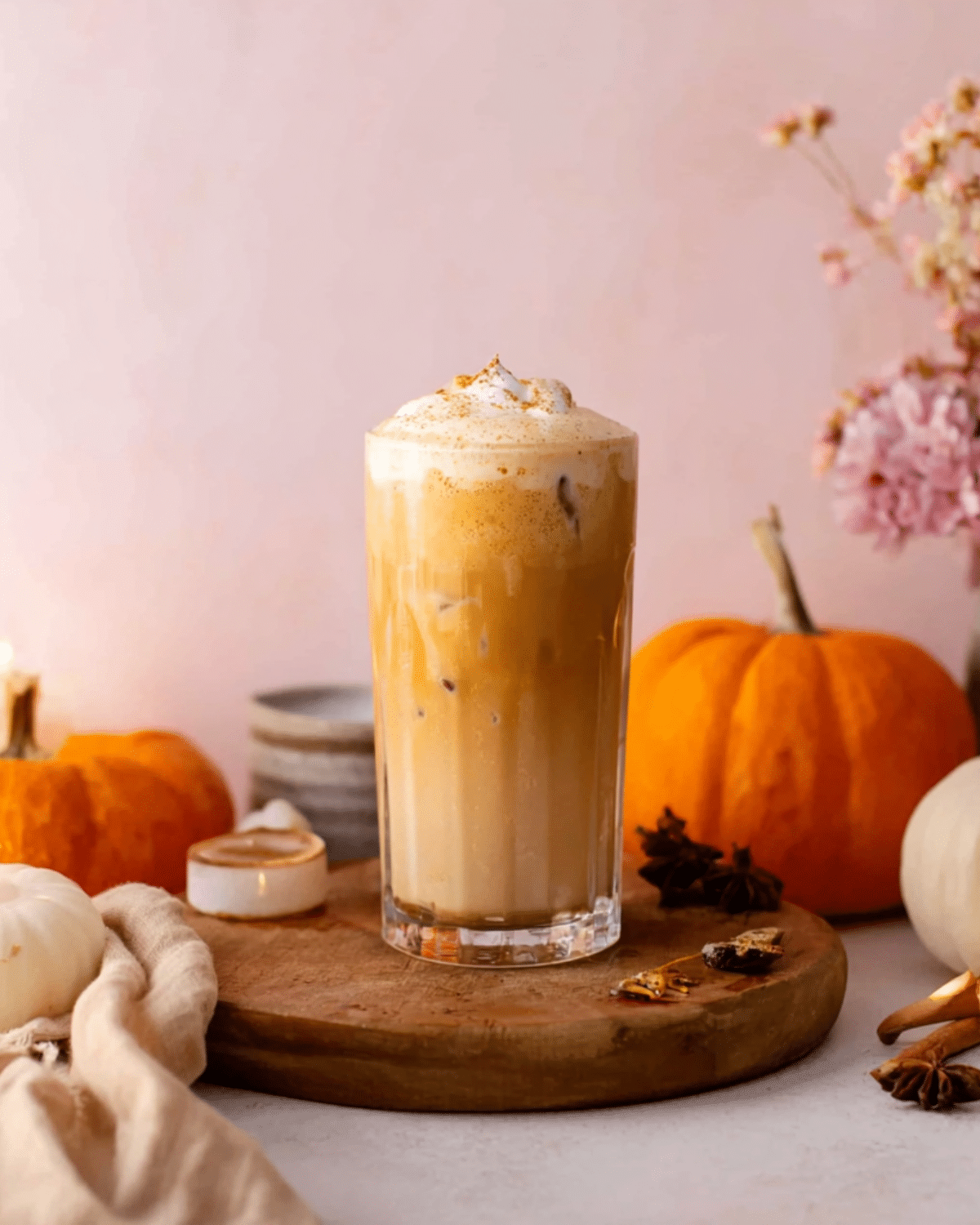 Pumpkin chai iced latte topped with creamy pumpkin foam and sprinkled with spices, served in a tall glass with autumn decor.