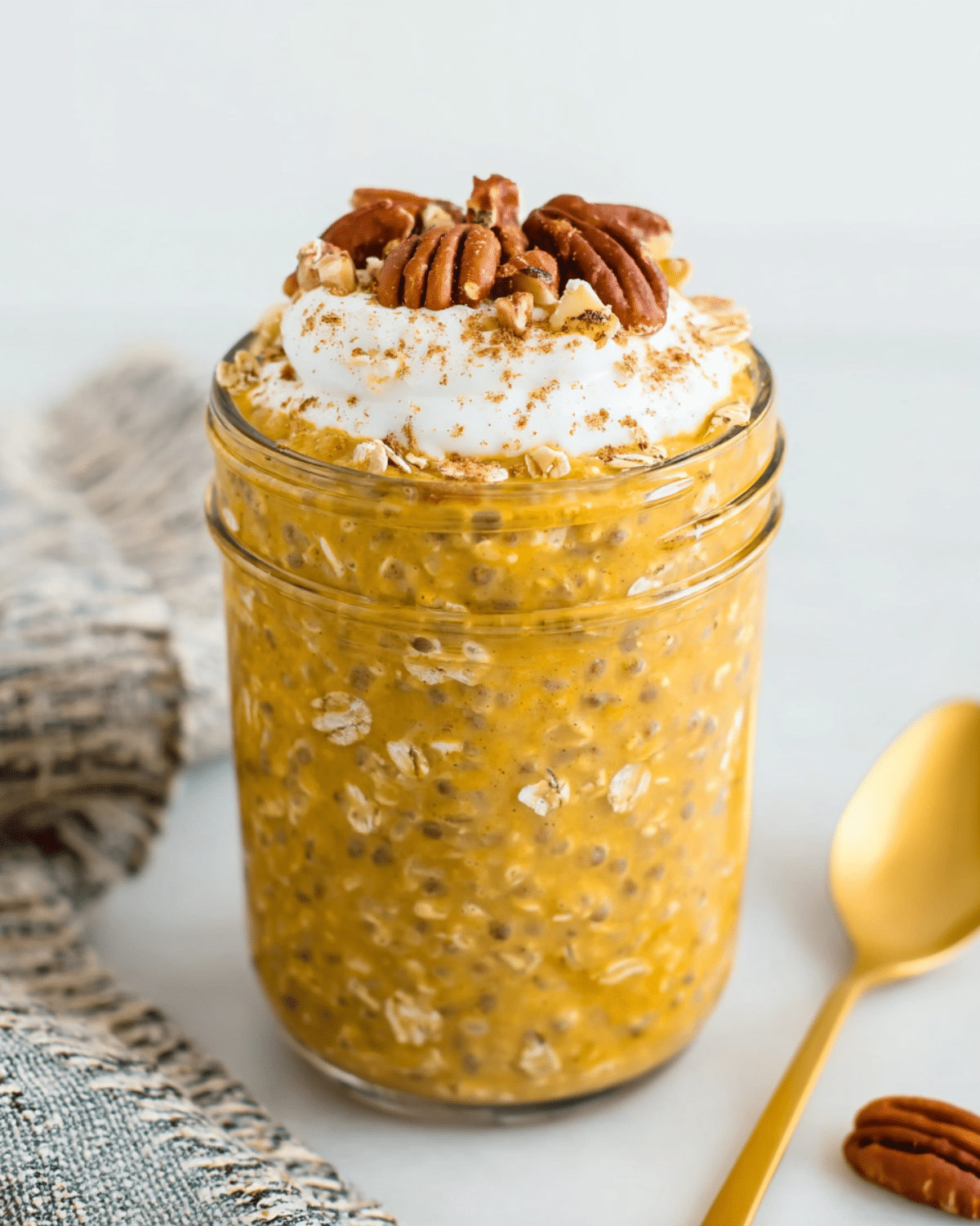 Pumpkin Pie Overnight Oats in a mason jar topped with whipped cream, pecans, and a sprinkle of cinnamon.