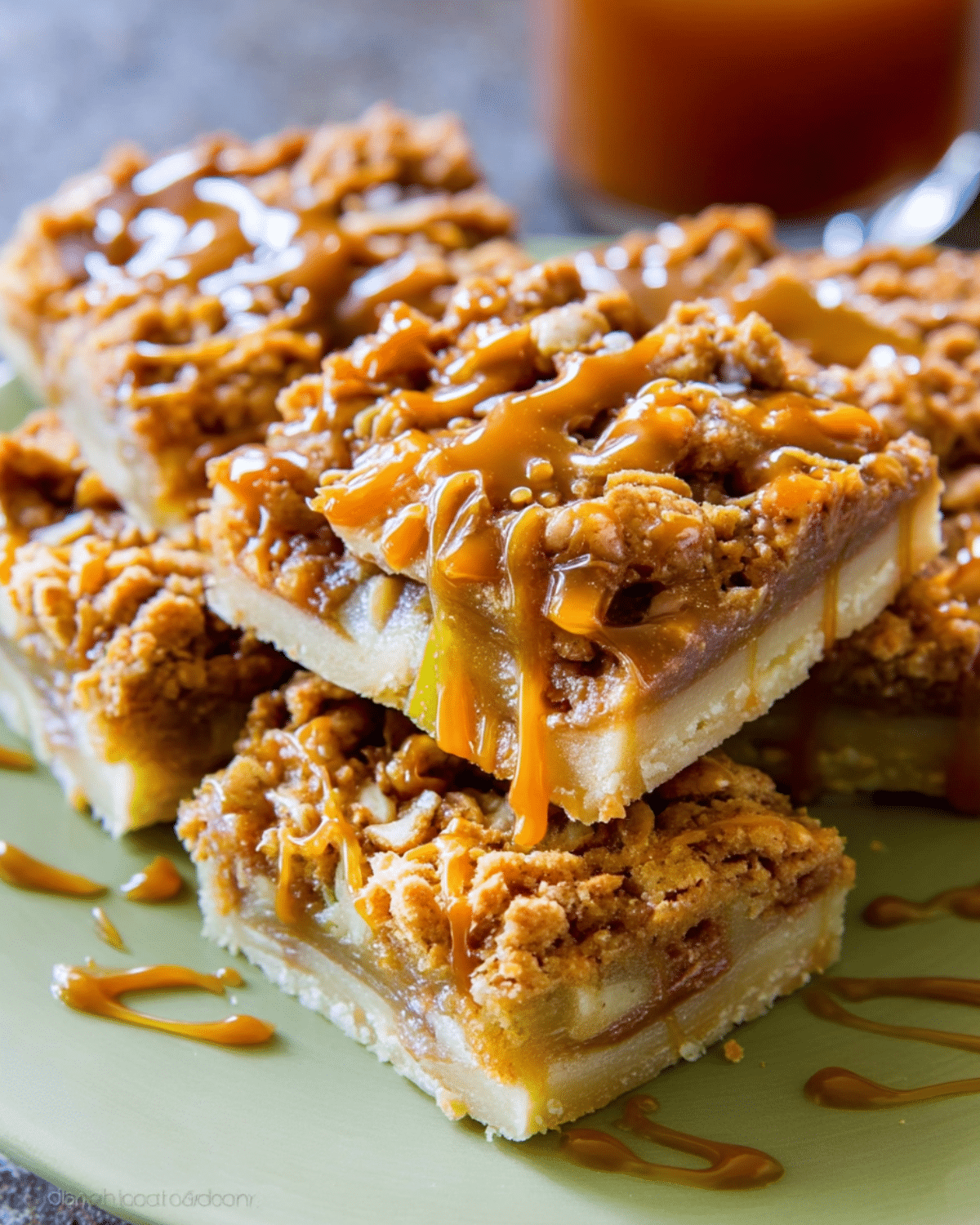 Salted Caramel Apple Pie Bars stacked on a green plate, drizzled with golden caramel sauce.