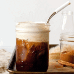 Mason jar filled with salted maple cinnamon cold brew, topped with a layer of cinnamon cream foam and served with a metal straw.
