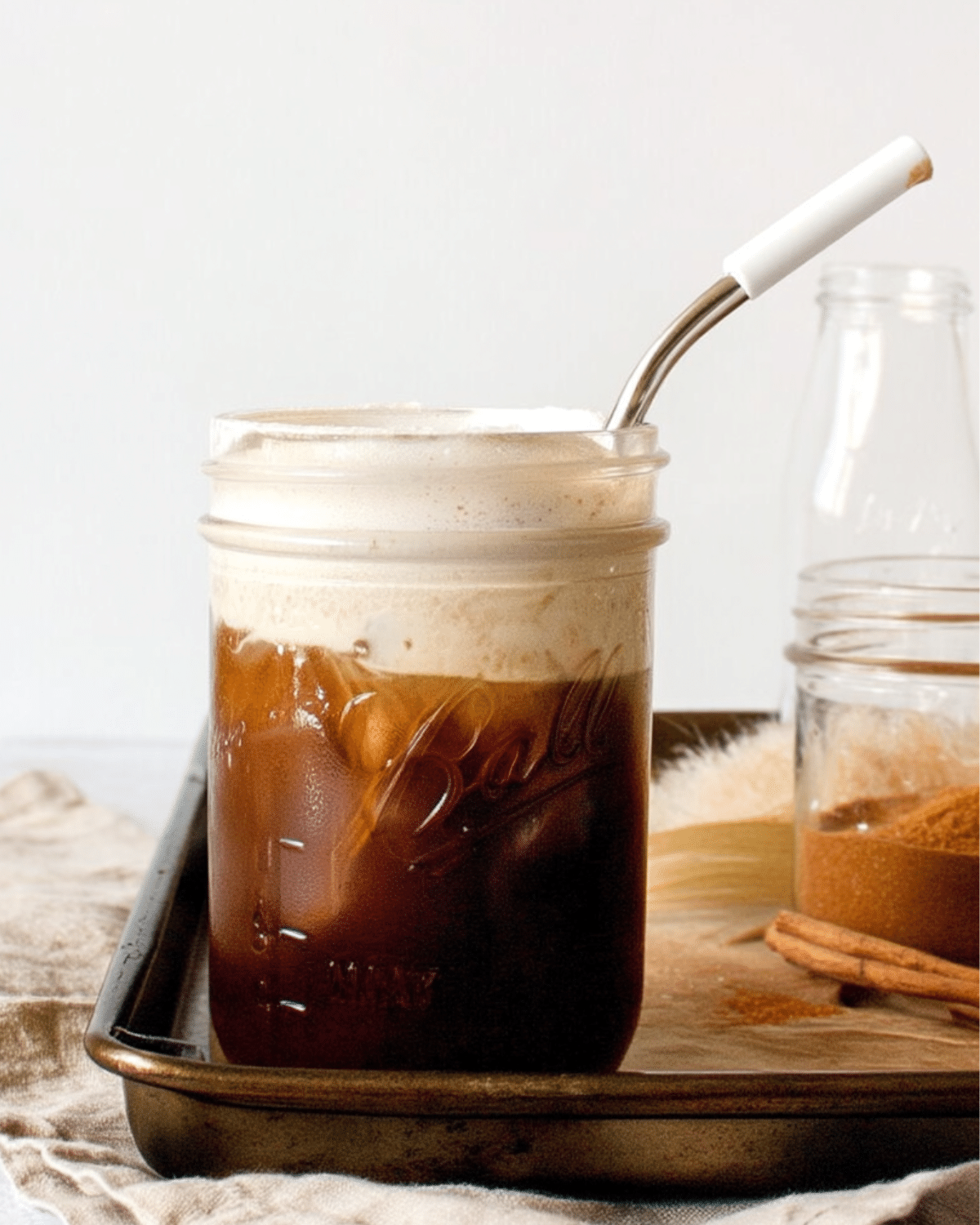 Mason jar filled with salted maple cinnamon cold brew, topped with a layer of cinnamon cream foam and served with a metal straw.