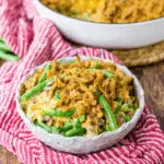Southern Green Bean Casserole topped with crispy fried onions, served in a rustic bowl on a red cloth.