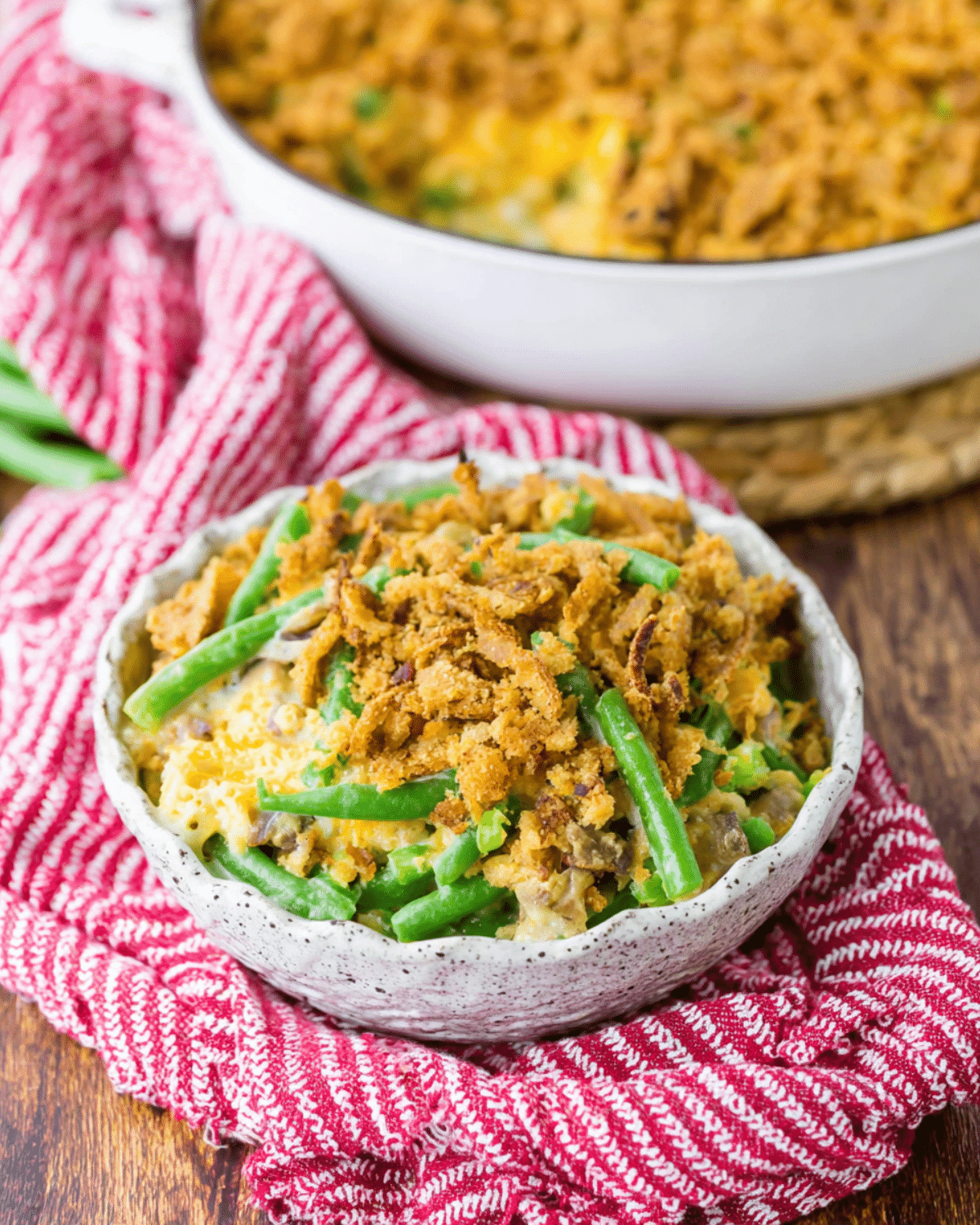 Southern Green Bean Casserole topped with crispy fried onions, served in a rustic bowl on a red cloth.