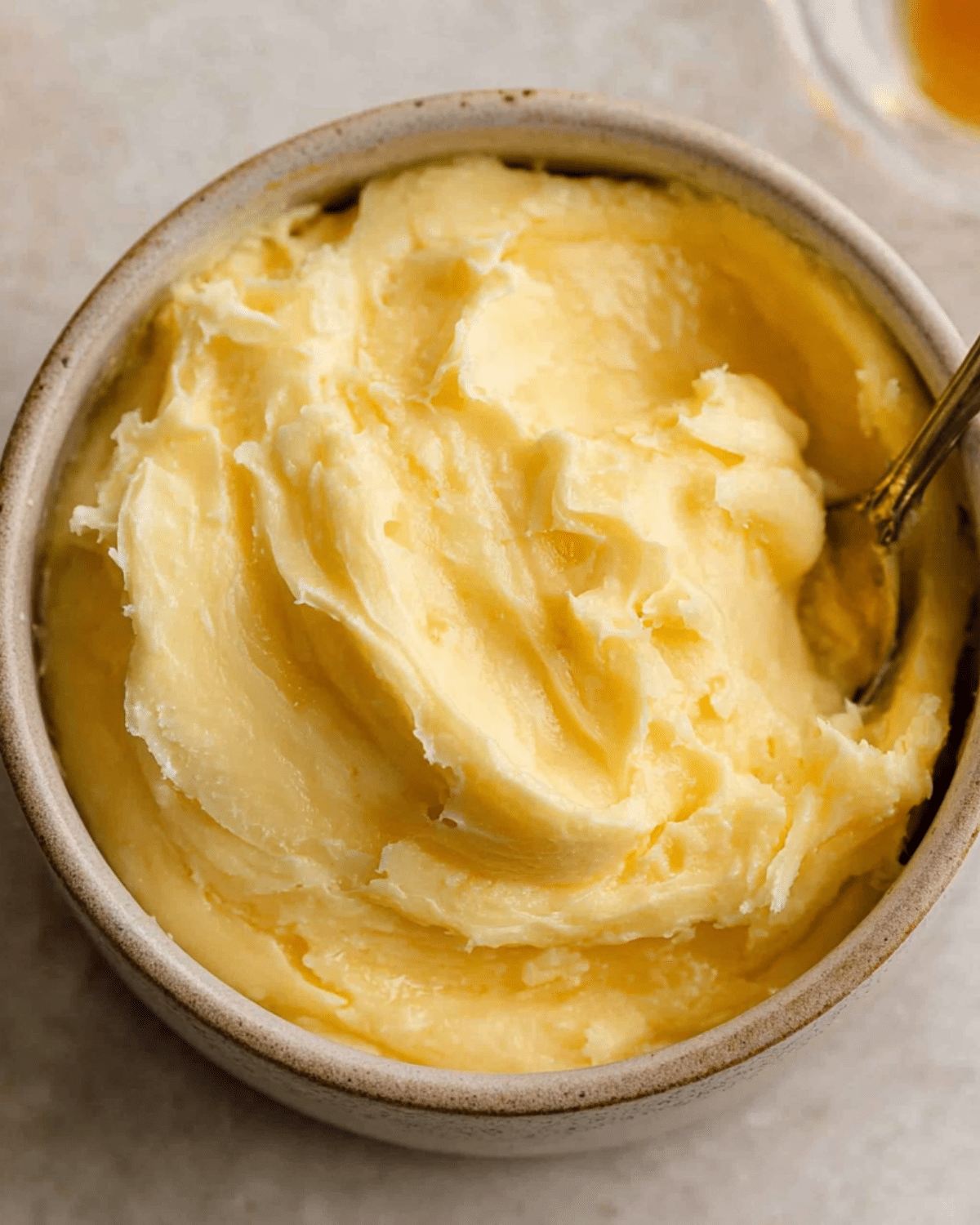 Creamy swirl of The BEST Honey Butter in a small ceramic bowl with a spoon.