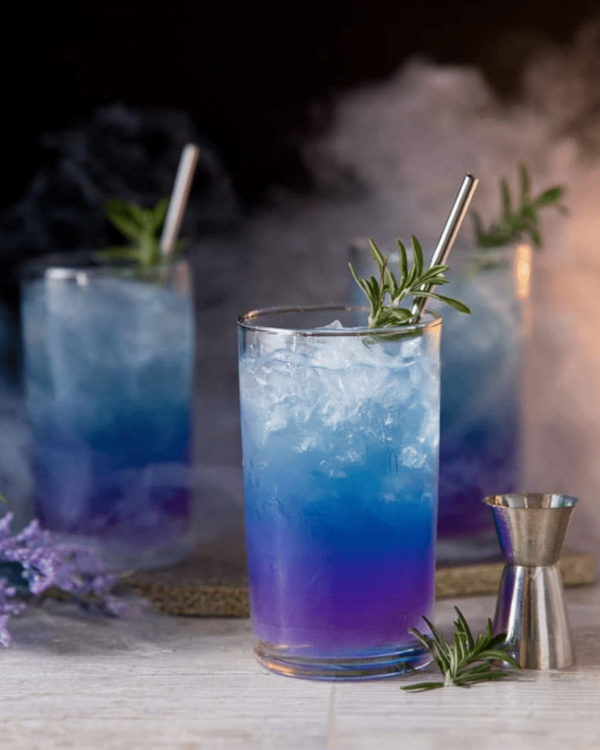 Vibrant Witches Brew Lemonade in tall glasses with crushed ice, garnished with rosemary and served with metal straws.
