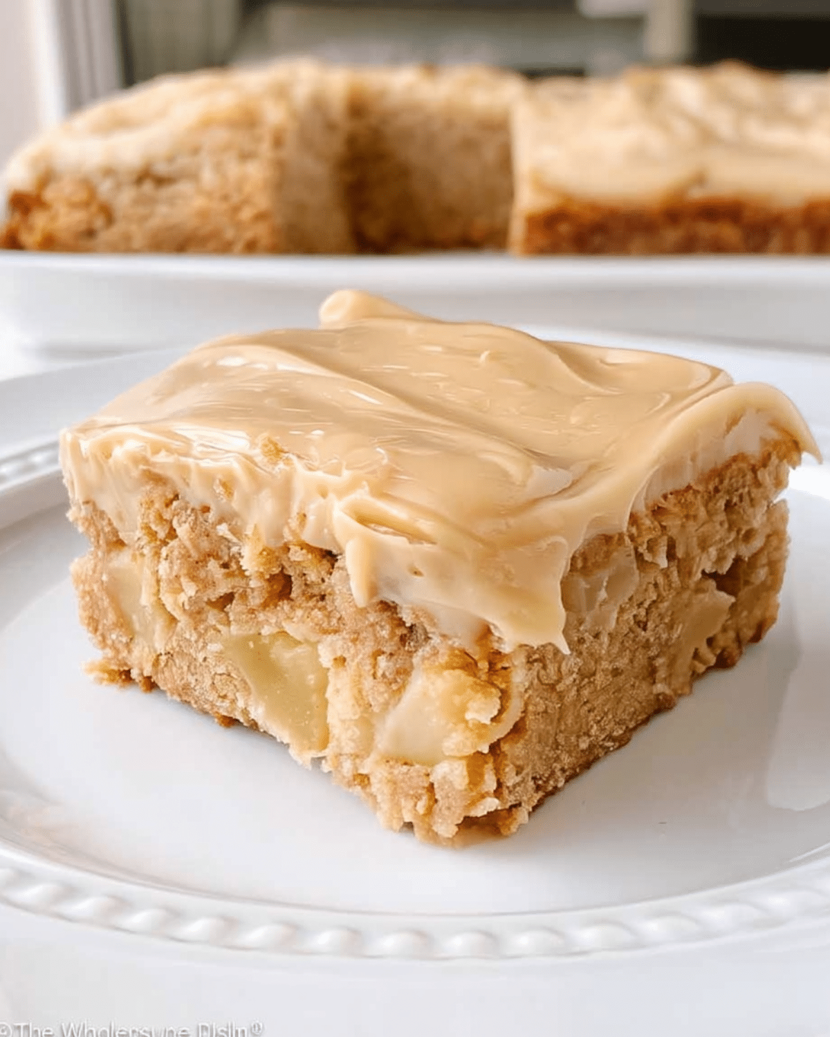Close-up of apple cinnamon blondies topped with maple cream cheese frosting on a white plate.