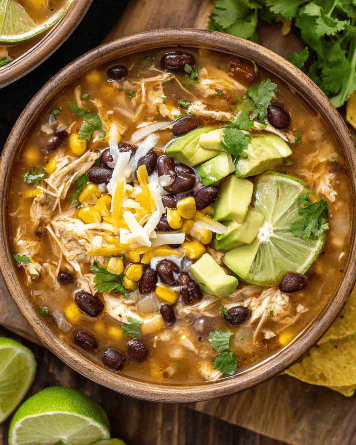A bowl of 7 Can Chicken Taco Soup topped with avocado, lime slices, shredded cheese, black beans, and corn.