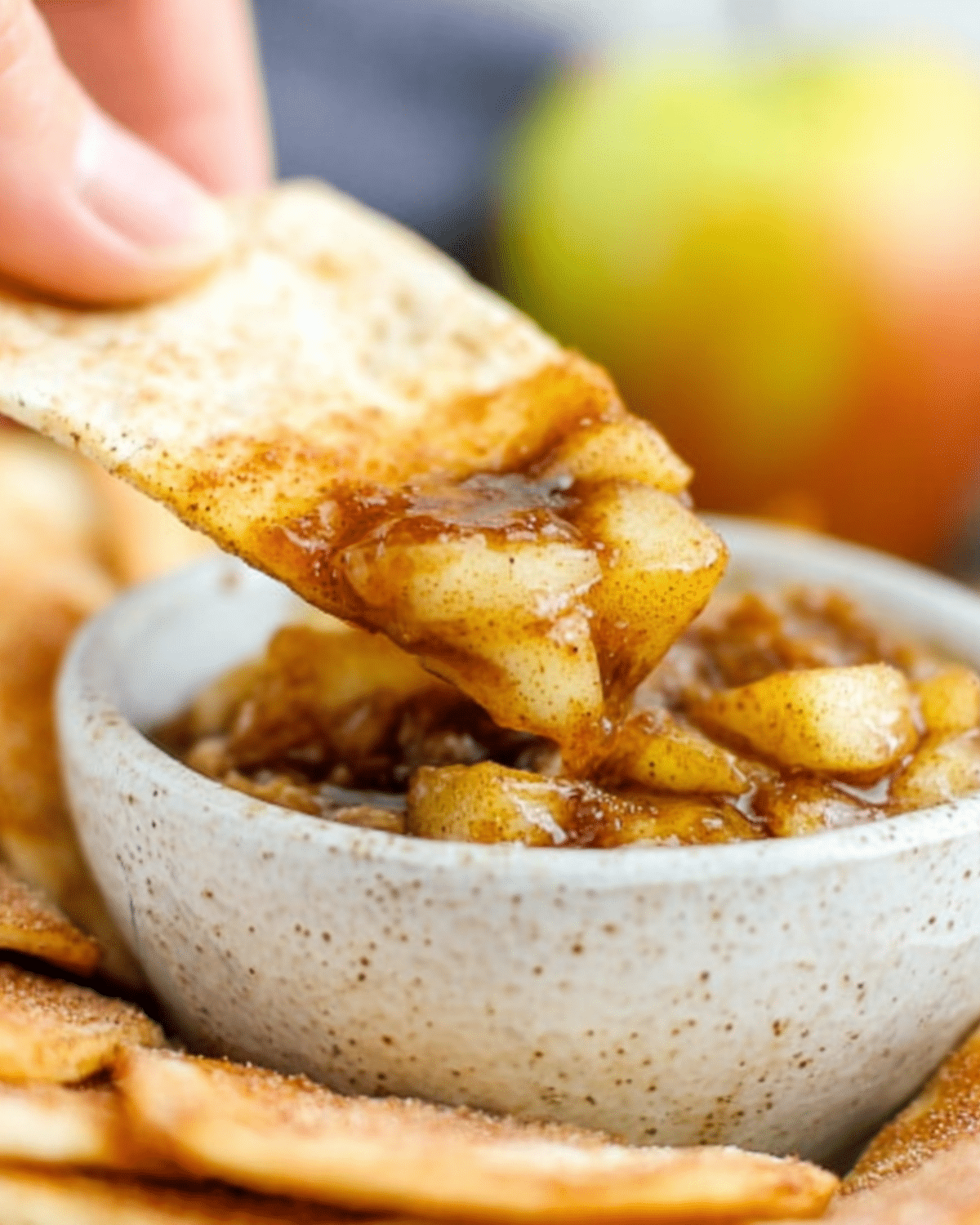 Close-up of apple pie dip with cinnamon sugar chips, featuring a chip scooping warm, spiced apple filling from a ceramic bowl.