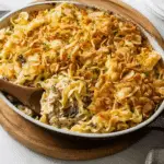 Baked tuna casserole topped with crispy fried onions and garnished with fresh chives, served in a white baking dish.
