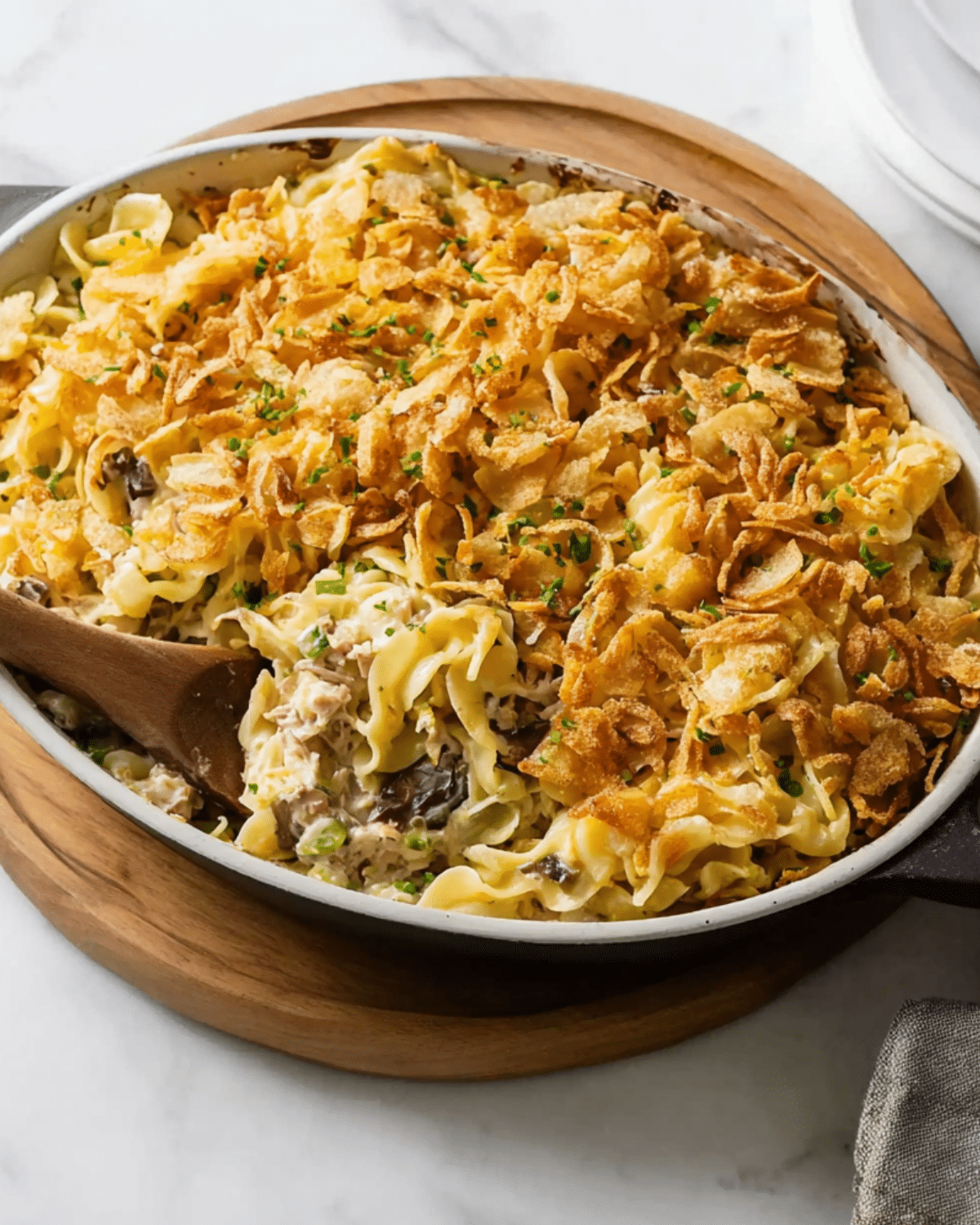 Baked tuna casserole topped with crispy fried onions and garnished with fresh chives, served in a white baking dish.