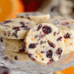 A stack of Cranberry Orange Shortbread Cookies displayed on a glass dessert stand with visible bits of dried cranberries and orange zest.