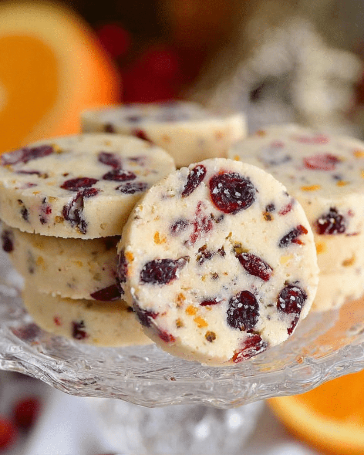 A stack of Cranberry Orange Shortbread Cookies displayed on a glass dessert stand with visible bits of dried cranberries and orange zest.