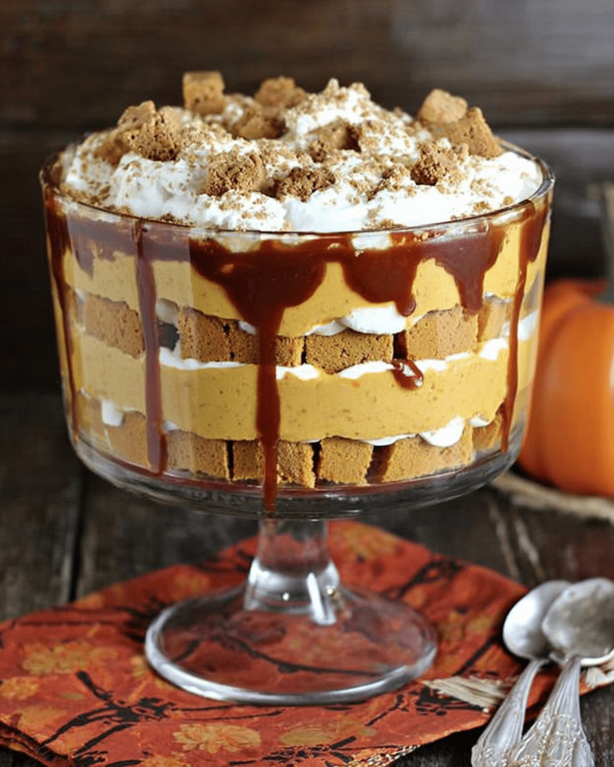 A glass trifle dish filled with layers of caramel, spiced pumpkin mousse, whipped cream, and gingersnap cookies, topped with crumbled cookies.