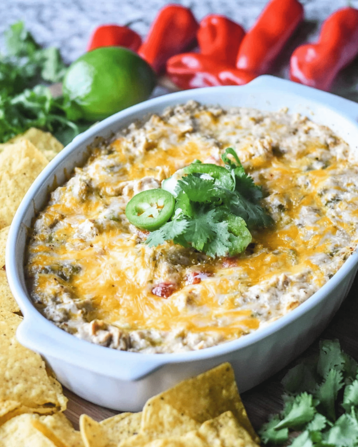 Baking dish filled with hot Cheesy Chicken Fajita Dip topped with melted cheese, jalapeño slices, and cilantro, served with tortilla chips.