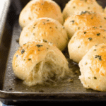 Tray of golden-brown Cheesy Garlic Bombs with melted cheese oozing out of one roll.