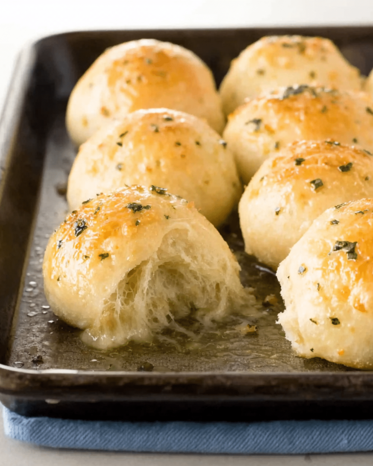 Tray of golden-brown Cheesy Garlic Bombs with melted cheese oozing out of one roll.