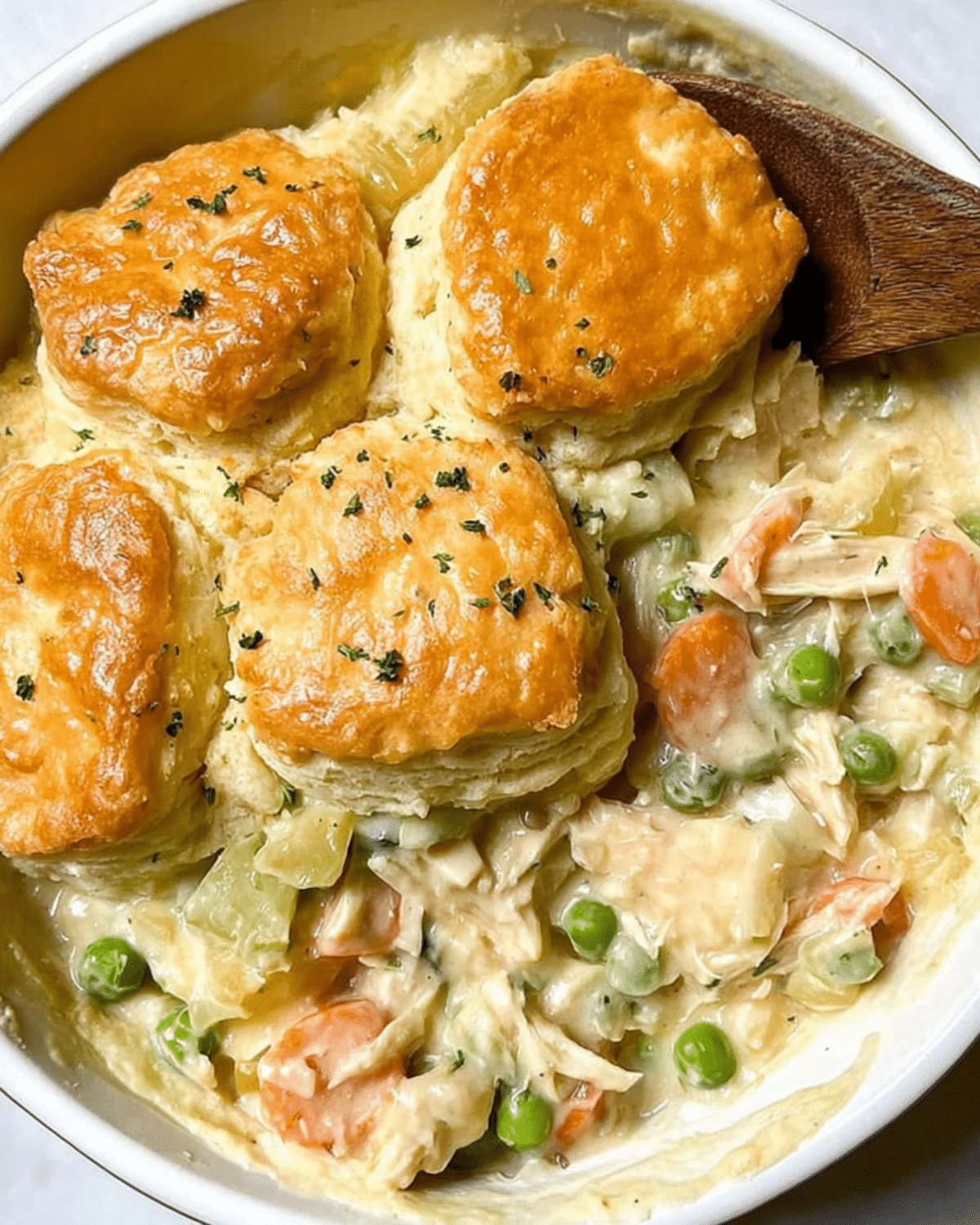 Chicken pot pie casserole with golden biscuits on top, filled with creamy chicken, peas, carrots, and celery.