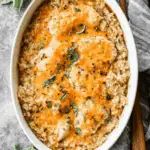 Baked chicken & rice casserole topped with melted cheese and garnished with fresh herbs in a white baking dish.