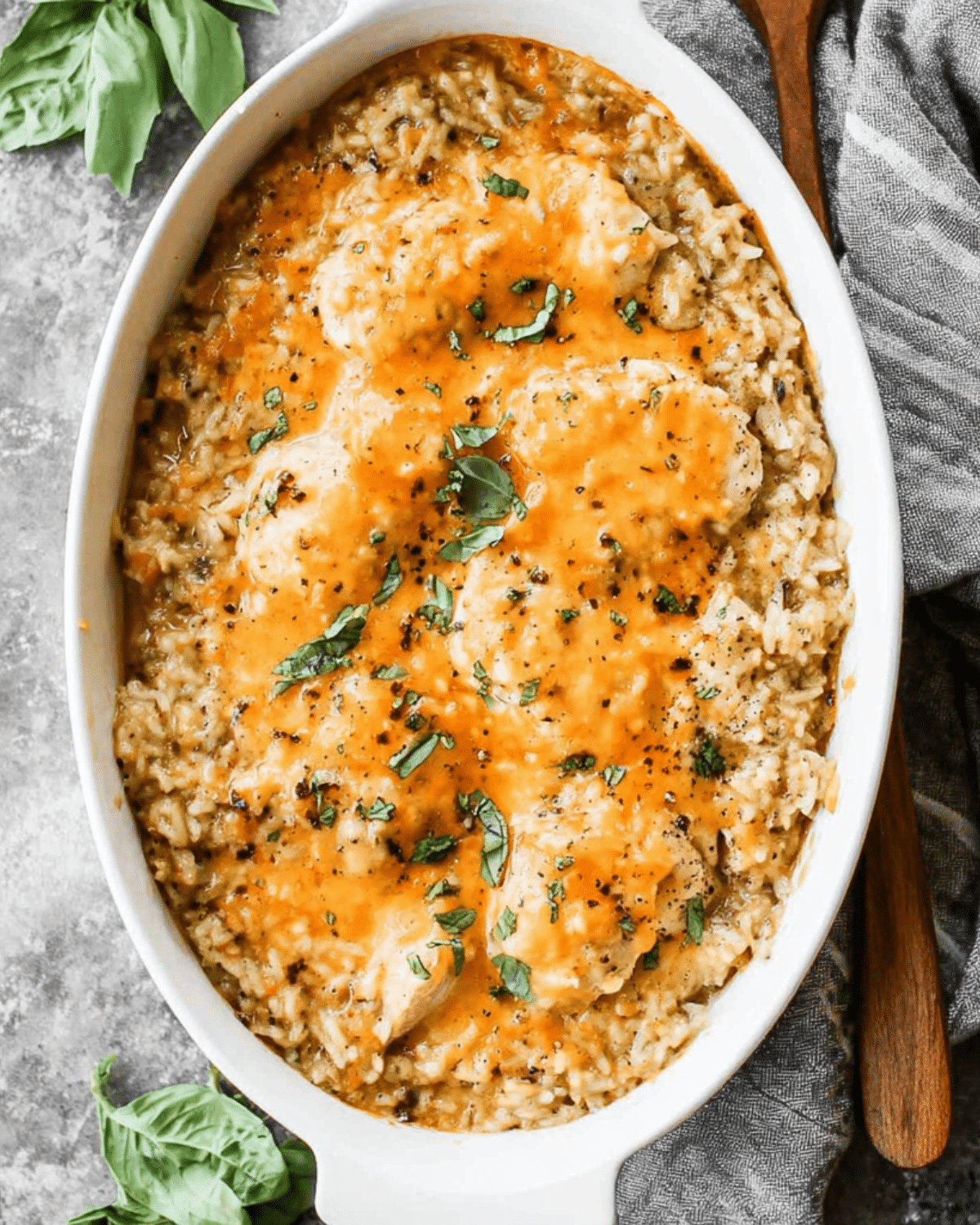 Baked chicken & rice casserole topped with melted cheese and garnished with fresh herbs in a white baking dish.