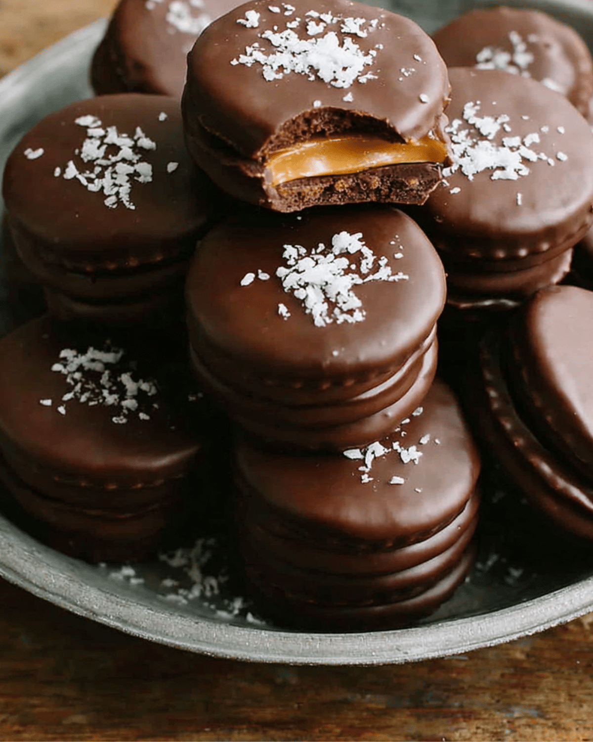 A plate stacked with chocolate peanut butter Ritz cookies, topped with sea salt and one with a bite showing the caramel and peanut butter filling.