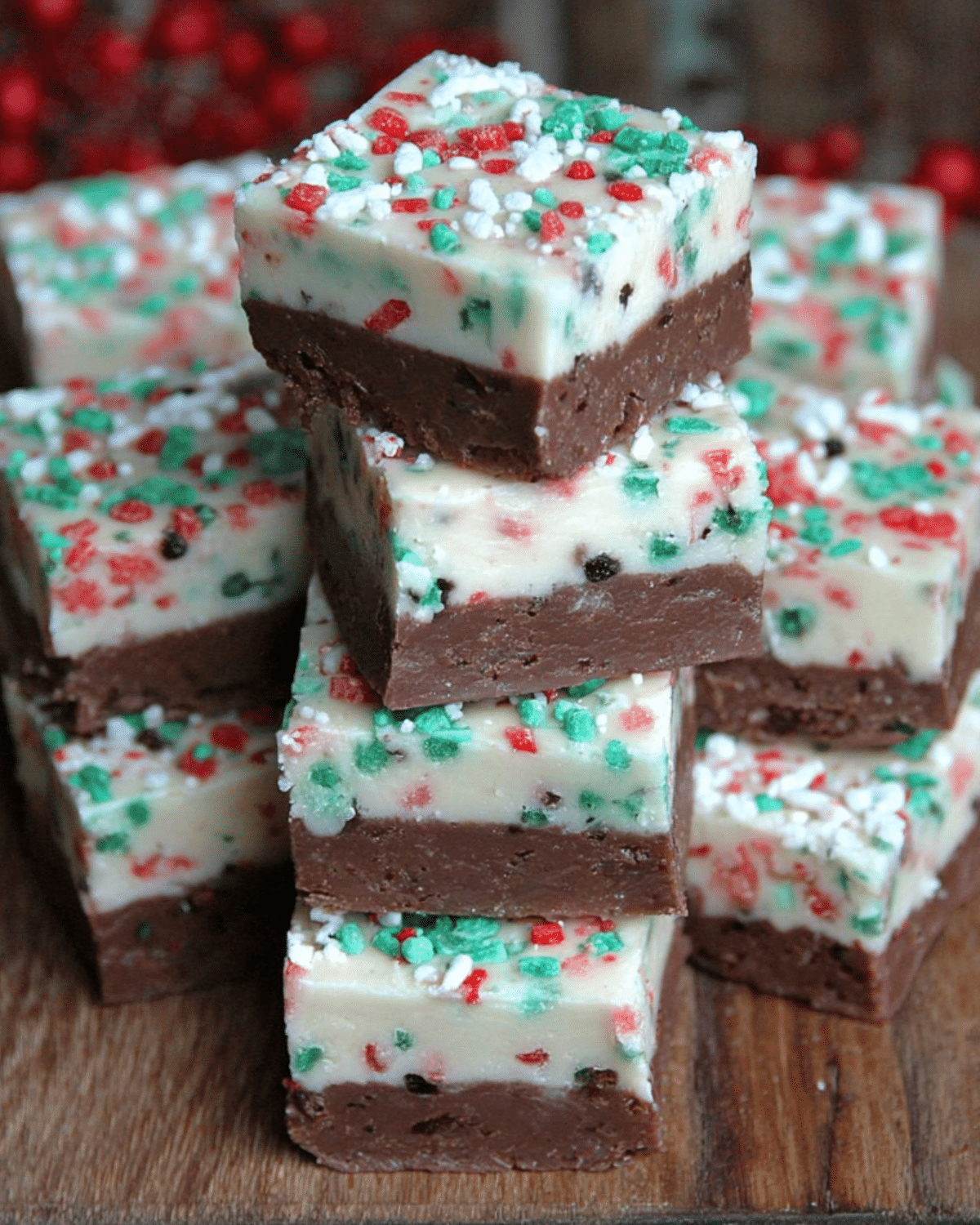 Stacked squares of Christmas fudge with a chocolate base and white top layer, decorated with red, green, and white holiday sprinkles.
