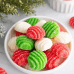 A bowl filled with red, green, and white Christmas mints coated in sugar with a ribbed swirl pattern.
