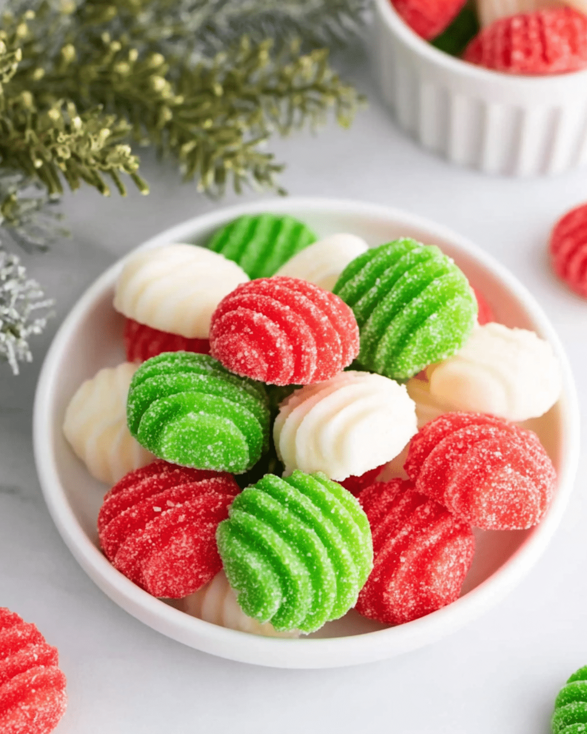 A bowl filled with red, green, and white Christmas mints coated in sugar with a ribbed swirl pattern.