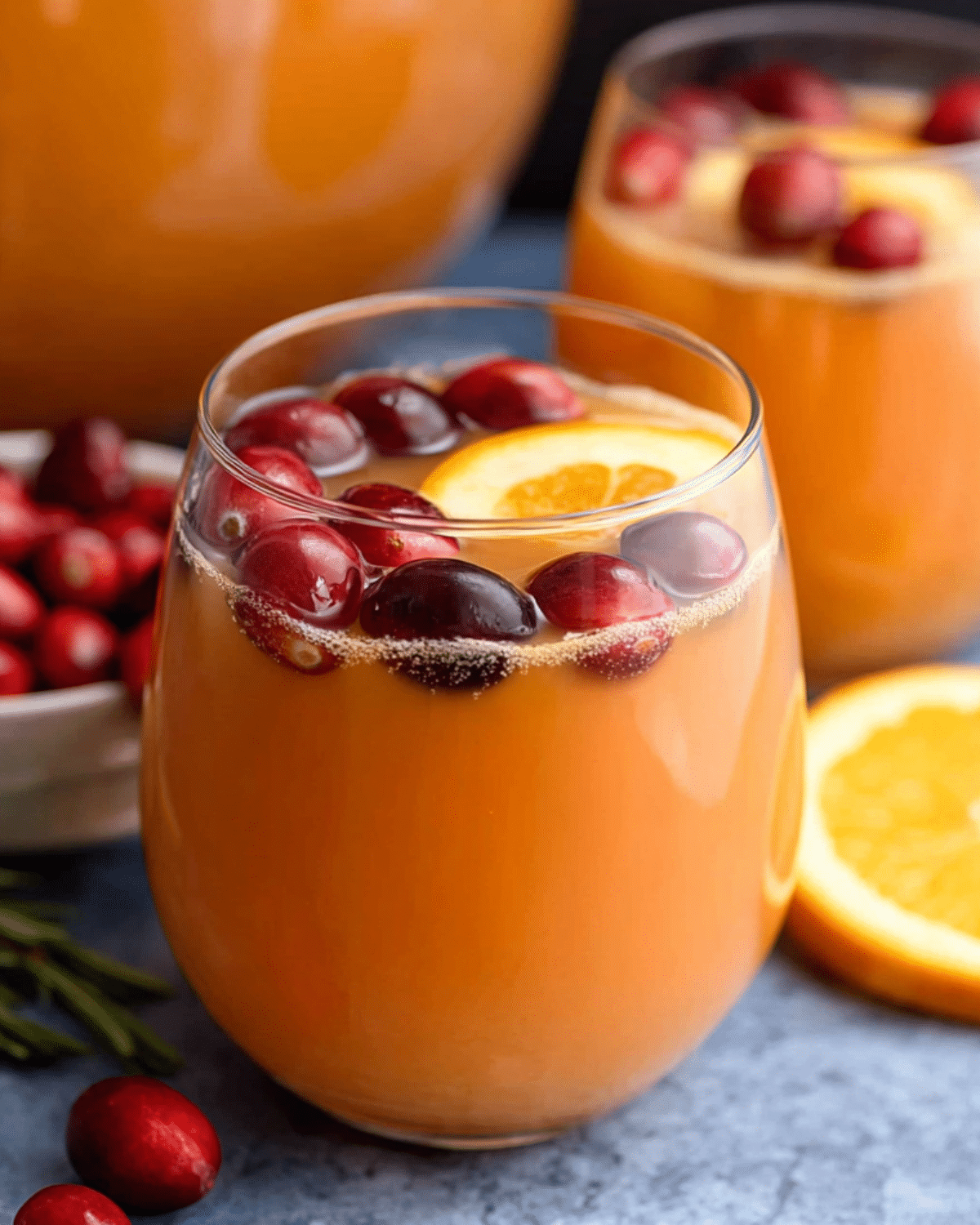 Glass of Christmas Morning Punch garnished with fresh cranberries and an orange slice, served chilled.