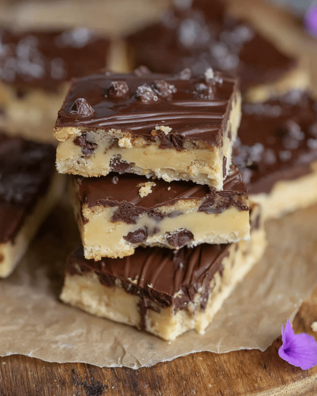 Stack of rich and gooey cookie dough bars topped with a thick layer of chocolate and chocolate chips.