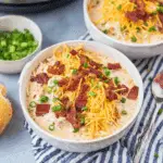 Two bowls of Crack Chicken Soup topped with crispy bacon, shredded cheddar cheese, and green onions.