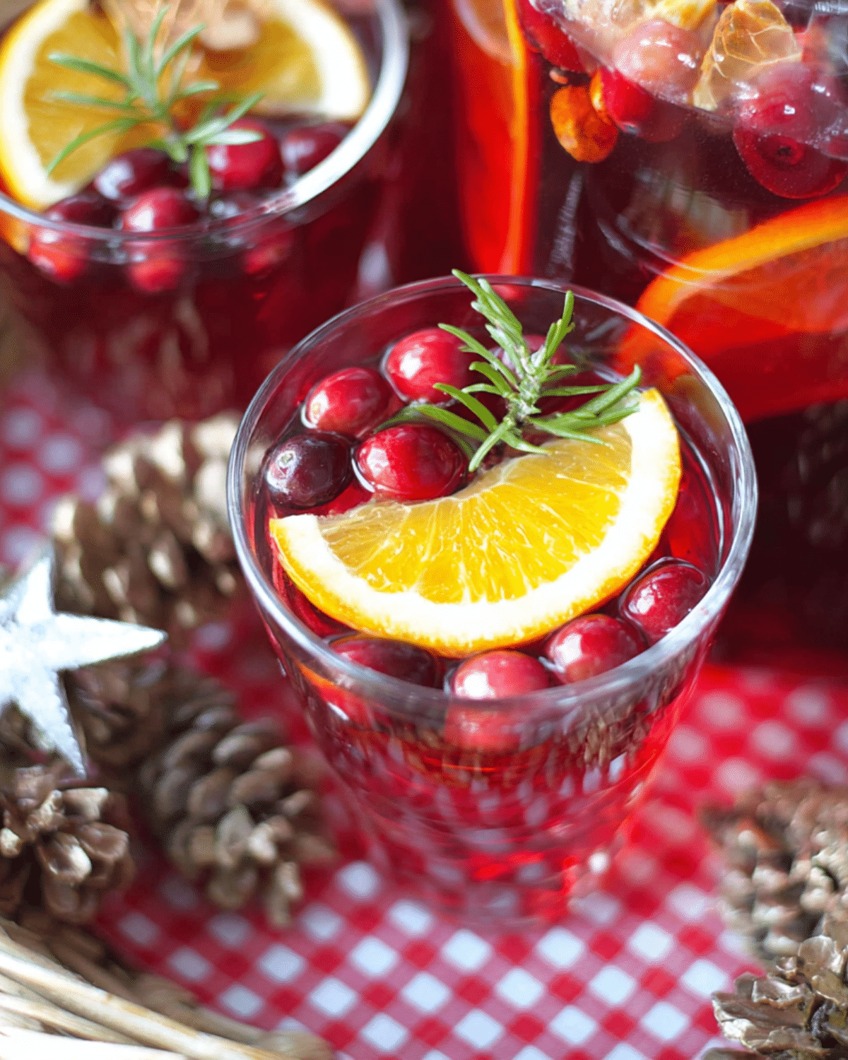 Glass of cranberry Christmas punch with ginger ale, garnished with fresh cranberries, an orange slice, and a sprig of rosemary.
