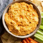 Crock Pot Buffalo Chicken Dip served in a rustic bowl, surrounded by tortilla chips, celery sticks, and carrot sticks for dipping.