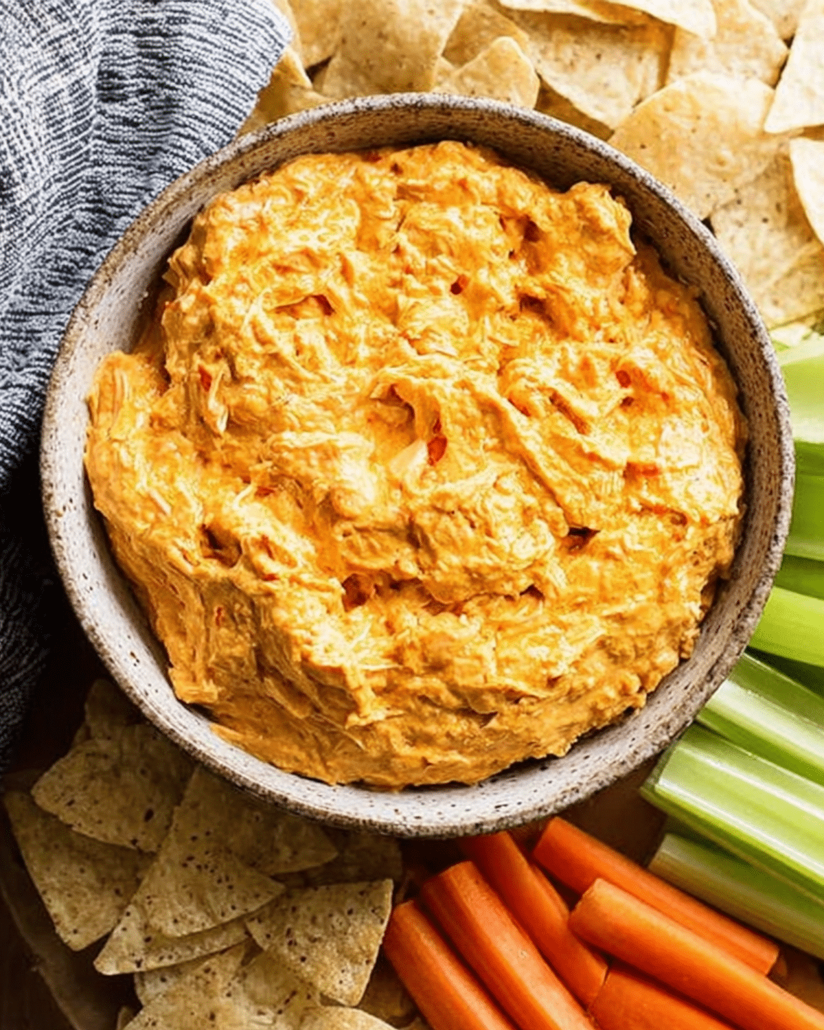 Crock Pot Buffalo Chicken Dip served in a rustic bowl, surrounded by tortilla chips, celery sticks, and carrot sticks for dipping.