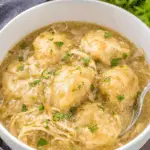 Crockpot Chicken and Dumplings in a white bowl, featuring tender shredded chicken, fluffy dumplings, and a creamy broth, garnished with fresh parsley.