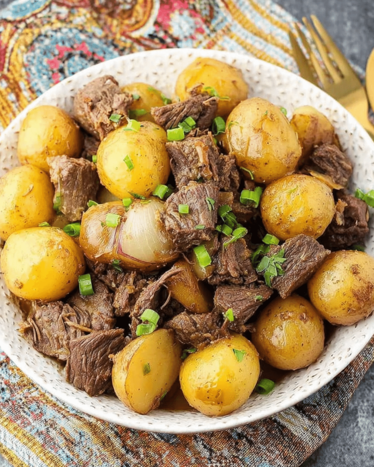 Crockpot Garlic Butter Beef Bites with Potatoes served in a white bowl, featuring tender beef chunks, golden baby potatoes, and onions, garnished with chopped green onions.