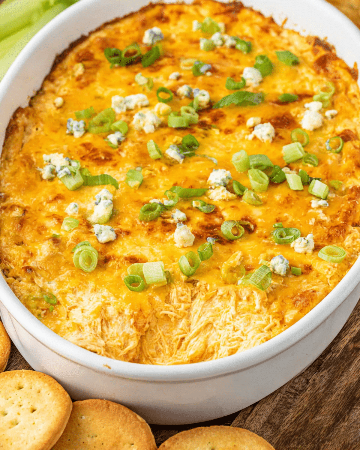 Frank’s Red Hot Buffalo Chicken Dip in a white baking dish, topped with melted cheese, green onions, and served with crackers.