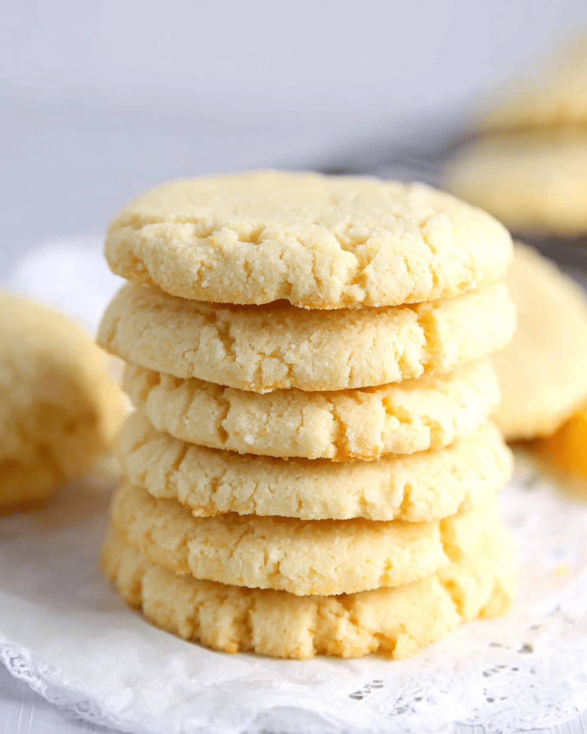 A stack of golden, soft-baked Grandma's sugar cookies arranged neatly on a lace-lined surface.
