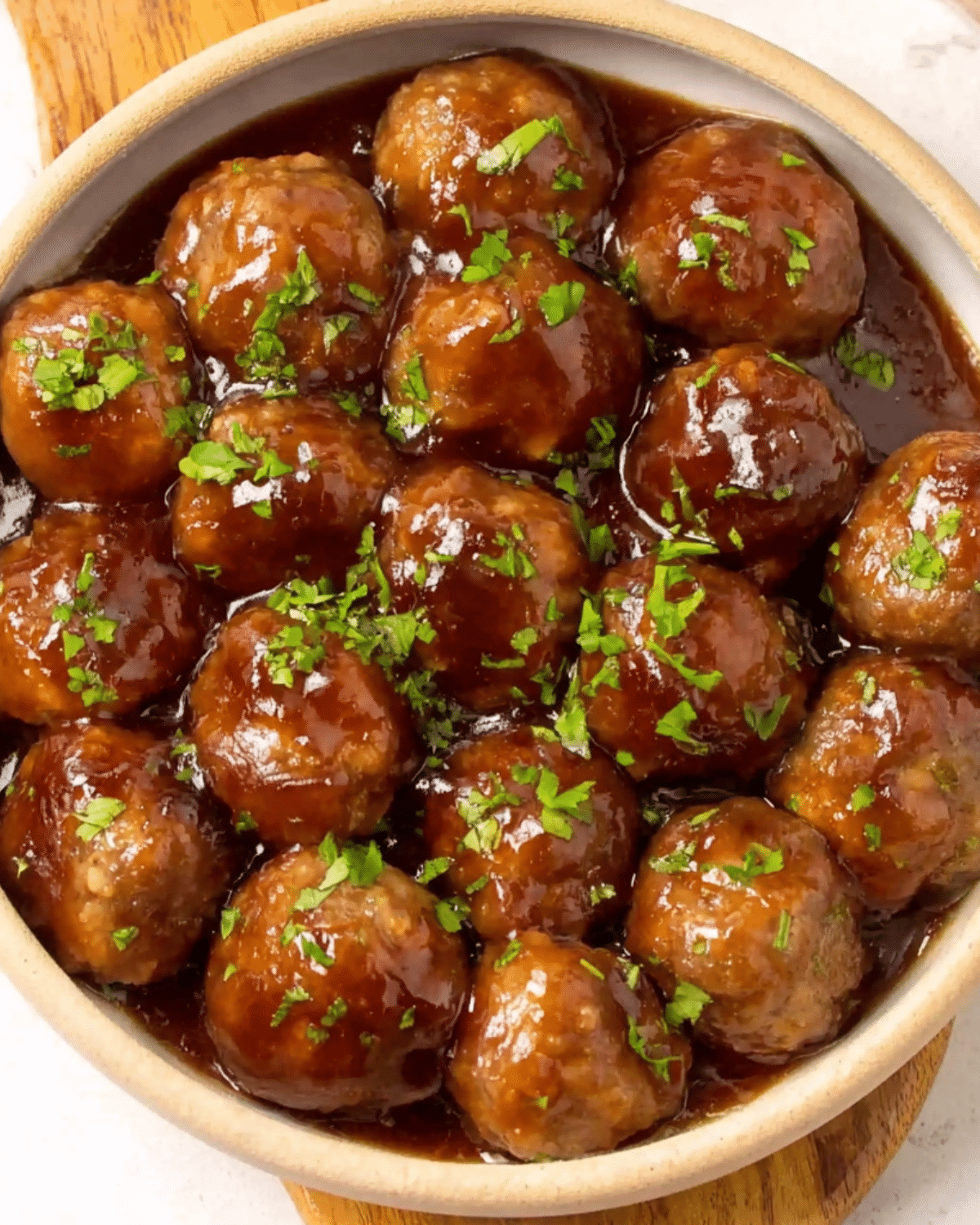 Bowl of grape jelly meatballs garnished with chopped parsley, coated in a glossy, sweet and tangy sauce.